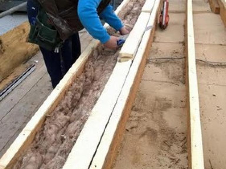 Perimeter insulation being laid inside the stripped roof joists
